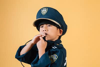 confident ethnic child in police uniform blowing whistle