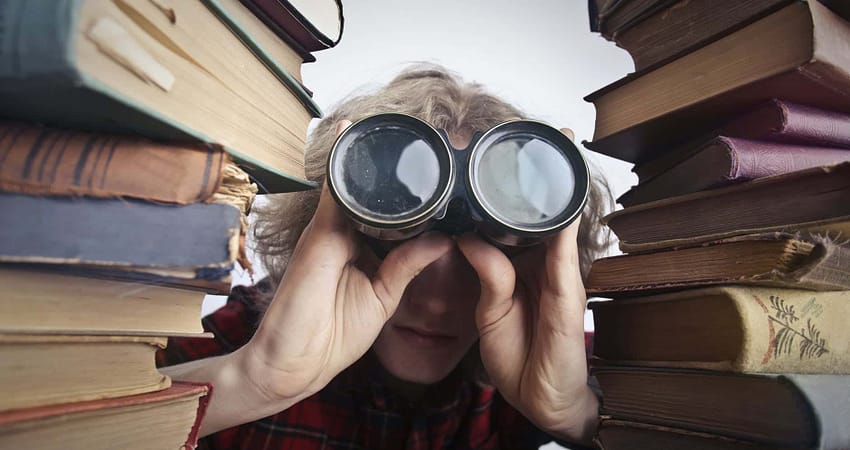 anonymous person with binoculars looking through stacked books