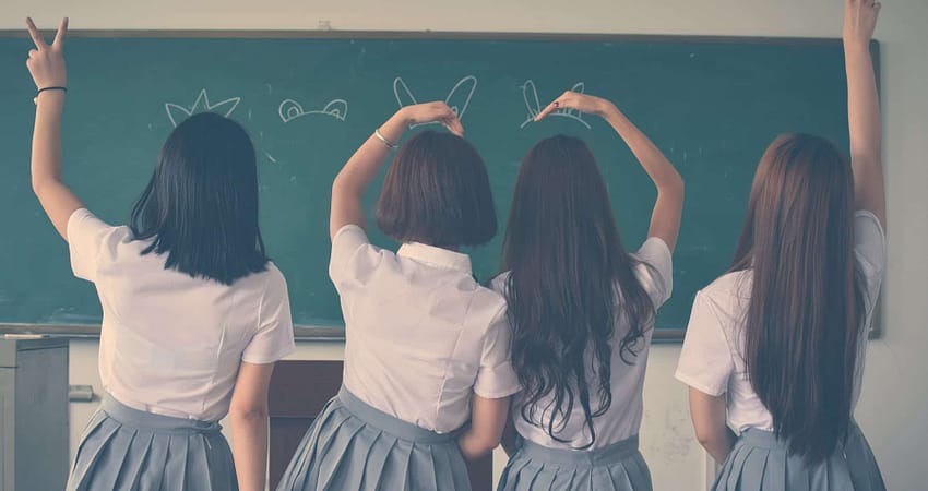 photo of four girls wearing school uniform doing hand signs